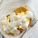 savory cornbread pancakes with eggs and country gravy on white plate with fork