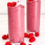 two pink smoothies on white table with raspberries
